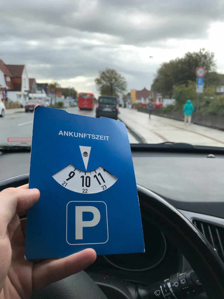 Neuer Bußgeldkatalog 2020: ein Autofahrer parkt auf einem Seitenstreifen und hält eine blaue Parkscheibe in der Hand.